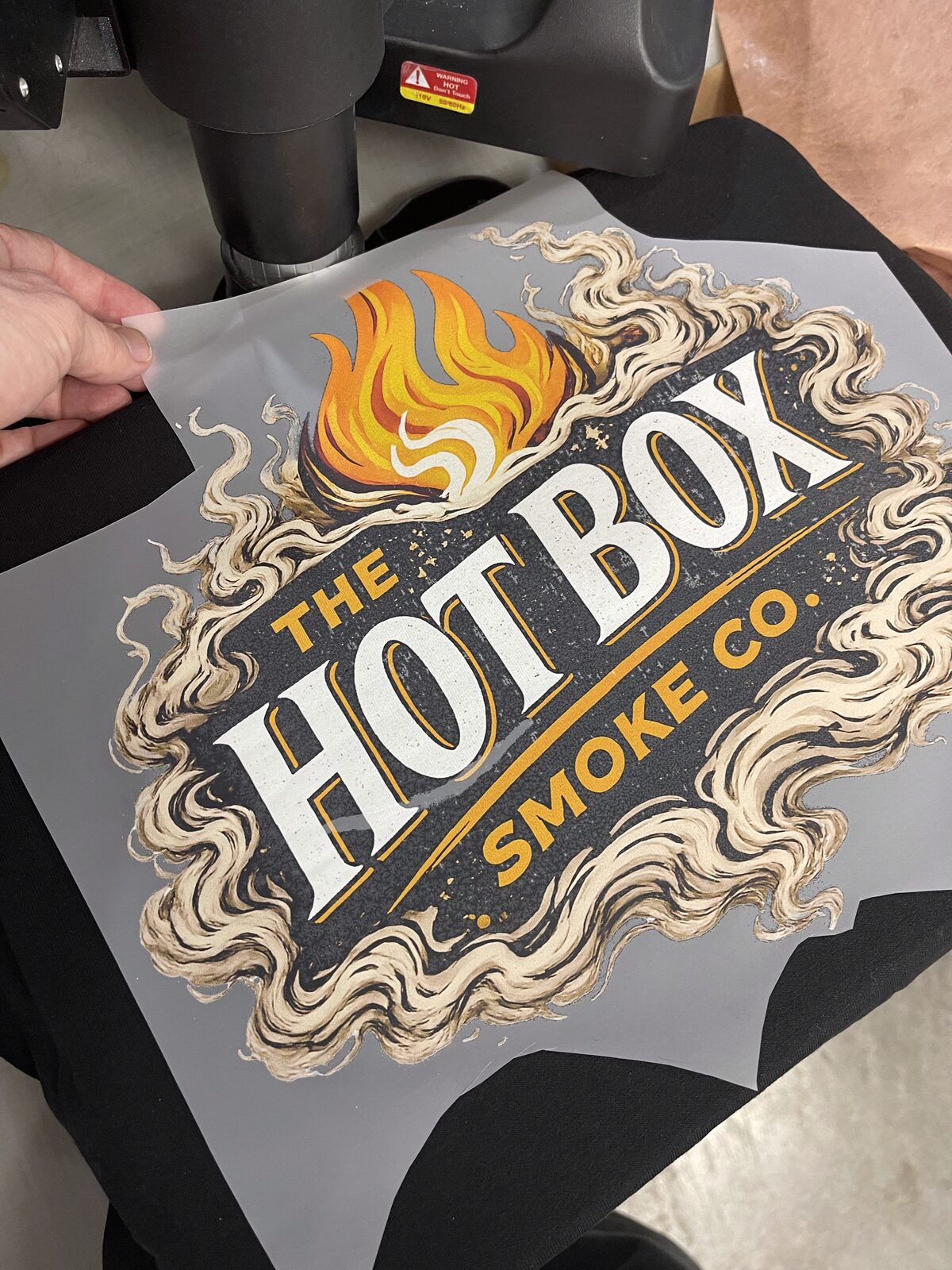 DTF transfer film with a flame and lettering design being peeled before pressing onto a garment